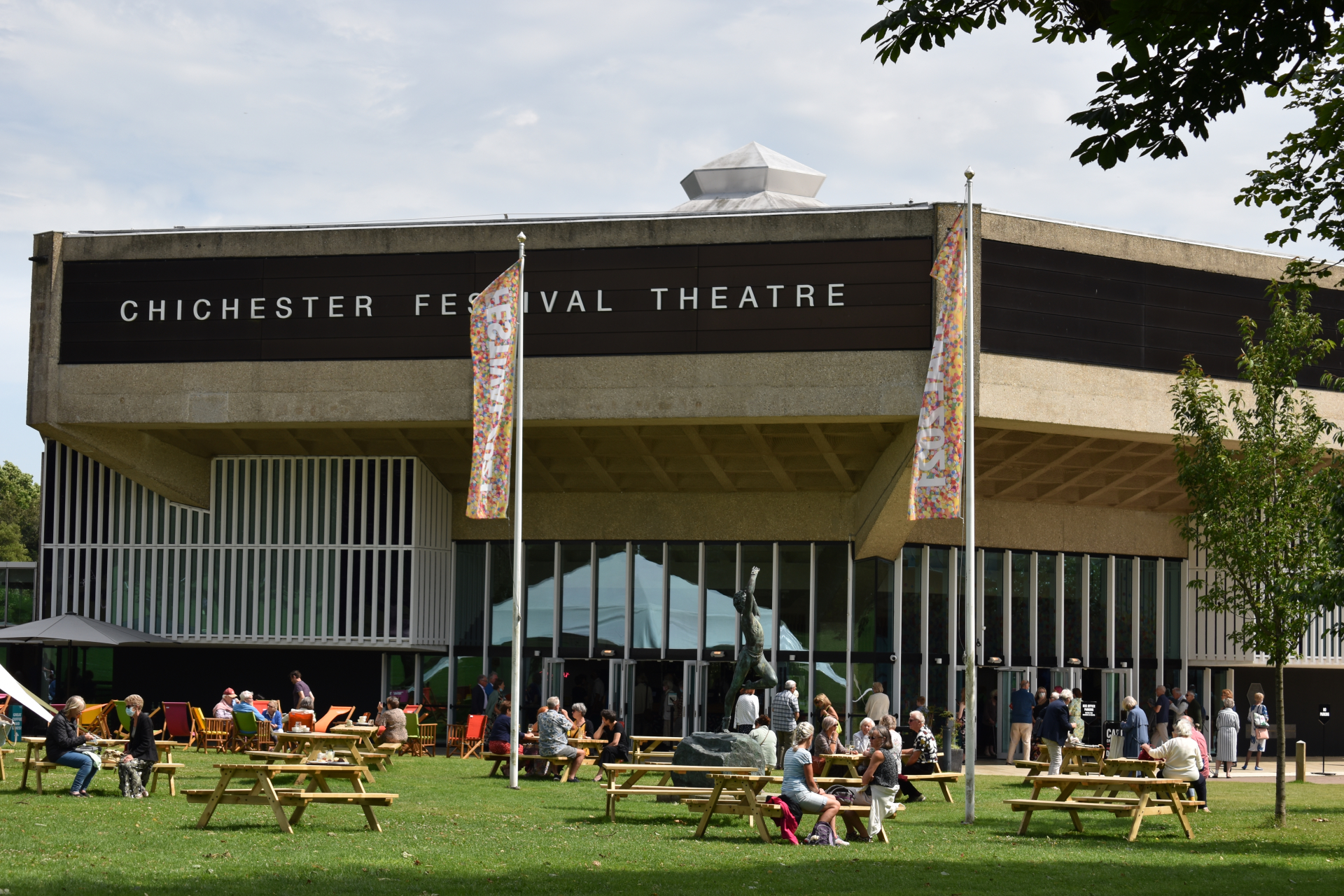 Image showing Chichester Festival Theatre on a sunny day with people seated at picnic tables on the grass in front.